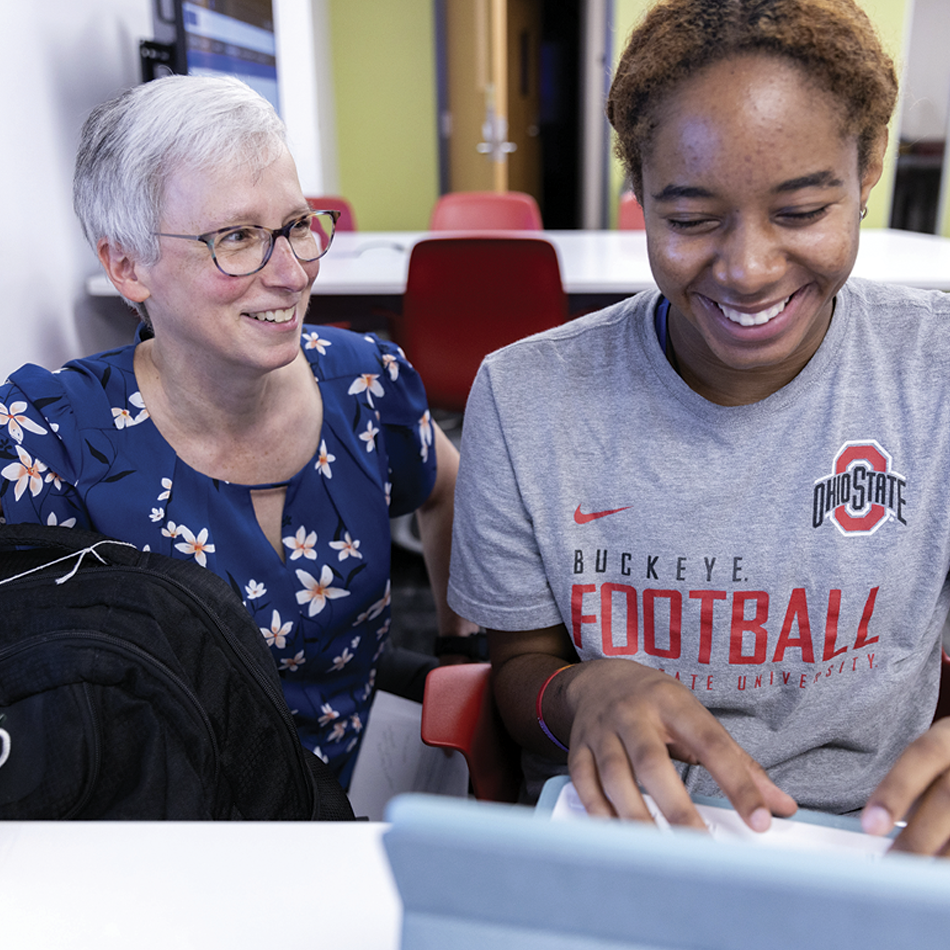 Student and guardian seated at a table, one using a tablet and smiling.