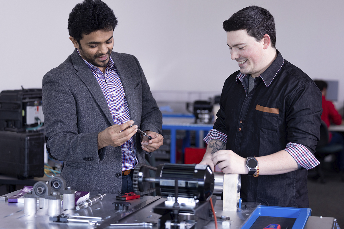 Two people collaborating in an engineering lab, examining a mechanical component on a table with tools and equipment.