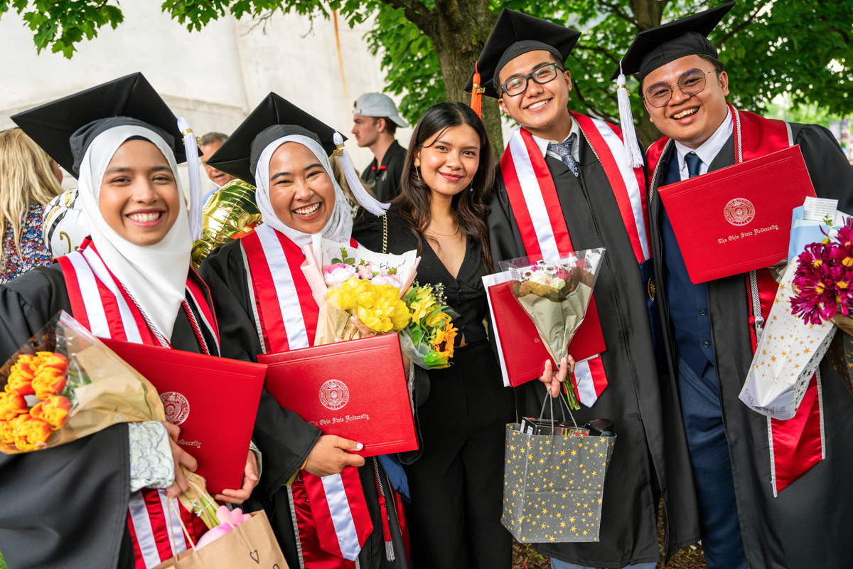 International students smiling with their diplomas at commencement