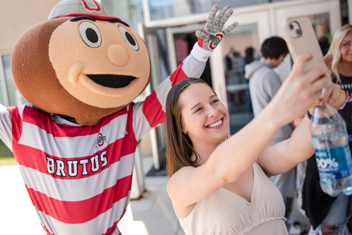 A student taking a selfie with Brutus Buckeye, the Ohio State University mascot