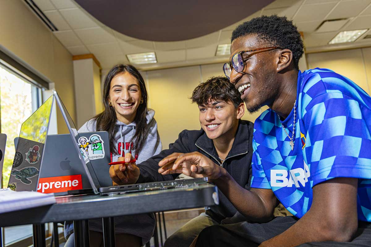 Two students watch another student work on a laptop
