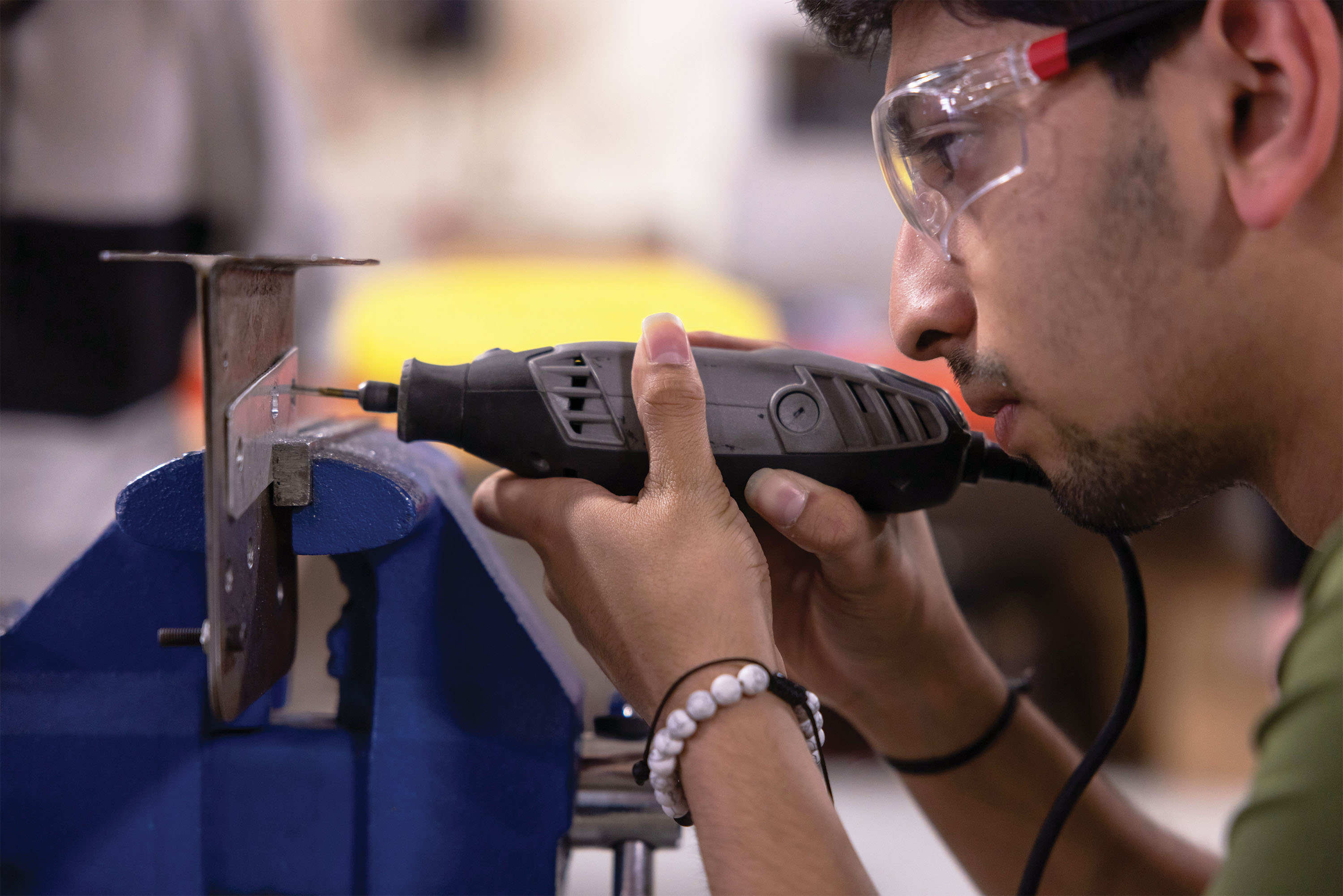 A college student drills a hole in a piece of metal for the breaking system of an automobile